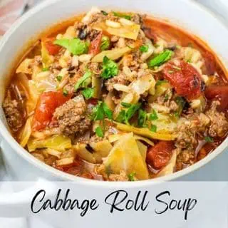 A bowl of cabbage roll soup with ground meat, chopped tomatoes, and rice, garnished with fresh parsley.