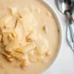 A bowl of Cabbage and Bean Soup with chunks of cabbage and chickpeas, placed on a marble surface next to a spoon and a striped napkin.