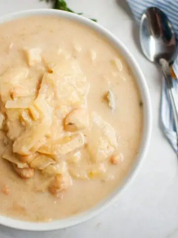 A bowl of Cabbage and Bean Soup with chunks of cabbage and chickpeas, placed on a marble surface next to a spoon and a striped napkin.