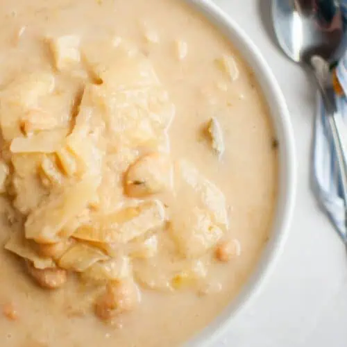 A bowl of Cabbage and Bean Soup with chunks of cabbage and chickpeas, placed on a marble surface next to a spoon and a striped napkin.