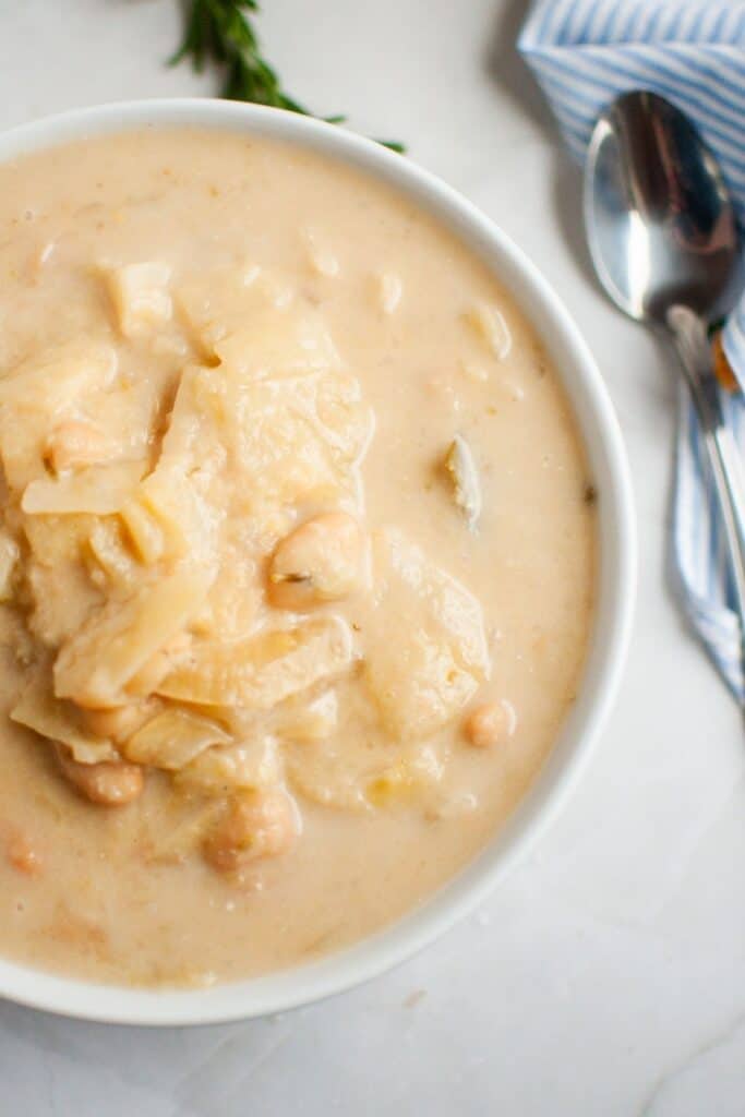 A bowl of Cabbage and Bean Soup with chunks of cabbage and chickpeas, placed on a marble surface next to a spoon and a striped napkin.