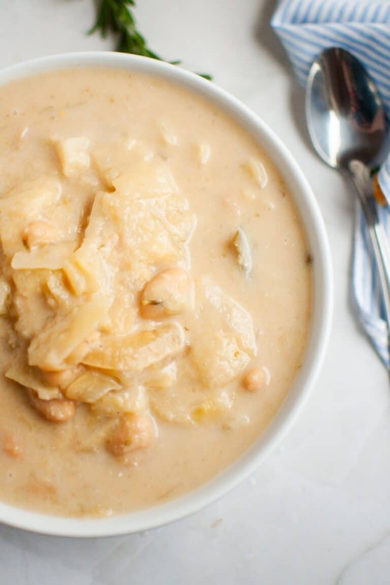 A bowl of Cabbage and Bean Soup with chunks of cabbage and chickpeas, placed on a marble surface next to a spoon and a striped napkin.