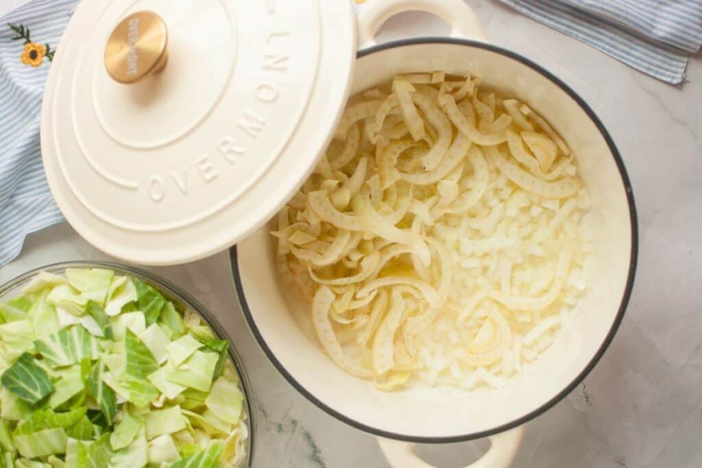 Pot of cooked onions and chopped cabbage on a table, next to a covered pot lid.