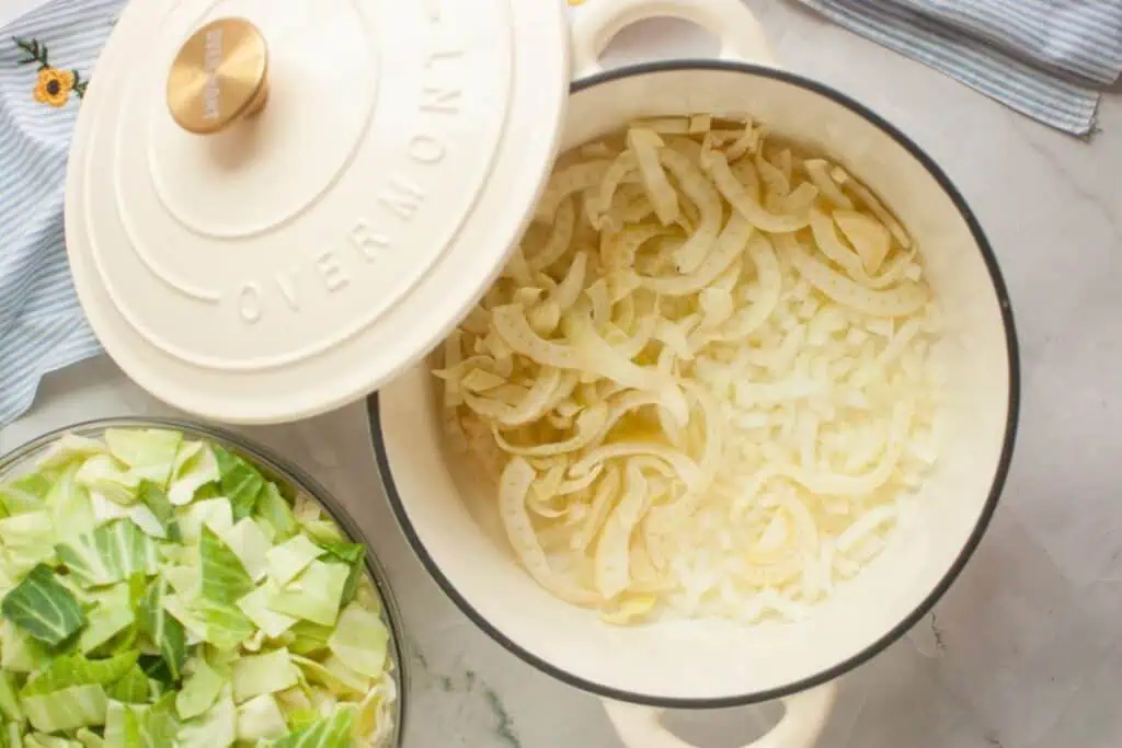 Pot of cooked onions and chopped cabbage on a table, next to a covered pot lid.