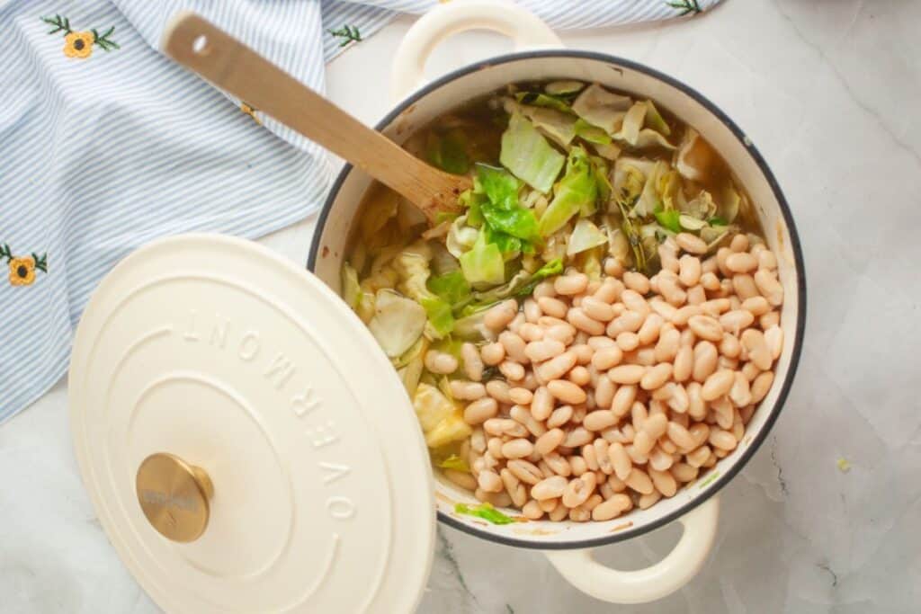 Pot of soup with white beans and cabbage, partially covered with a white lid.