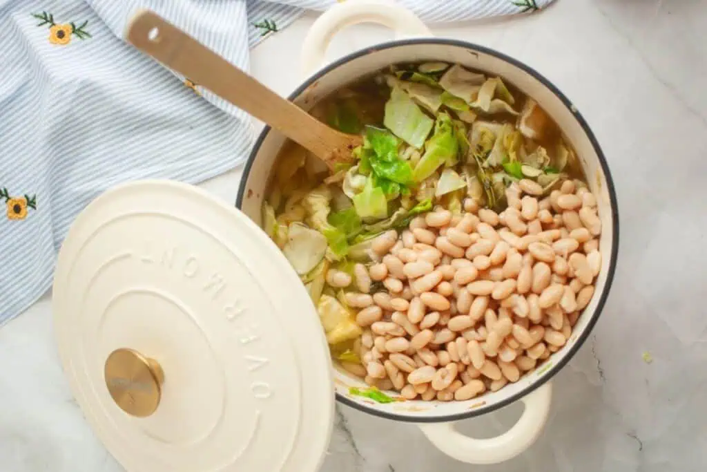Pot of soup with white beans and cabbage, partially covered with a white lid.