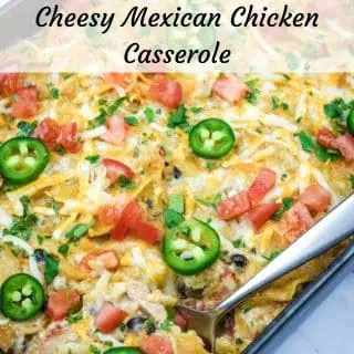 A Cheesy Mexican Casserole topped with melted cheese, jalapeño slices, diced tomatoes, and chopped herbs, with a serving spoon placed on the side.