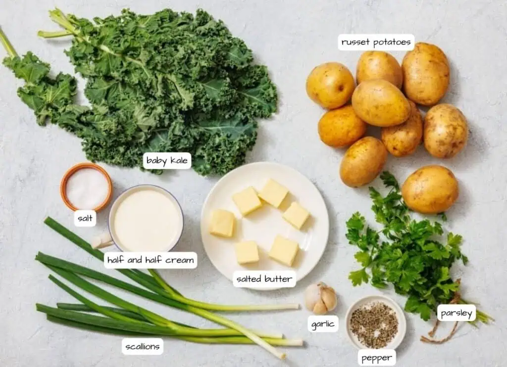 Ingredients for Colcannon with Kale on a surface include baby kale, russet potatoes, scallions, half and half cream, salted butter, parsley, garlic, salt, and pepper.