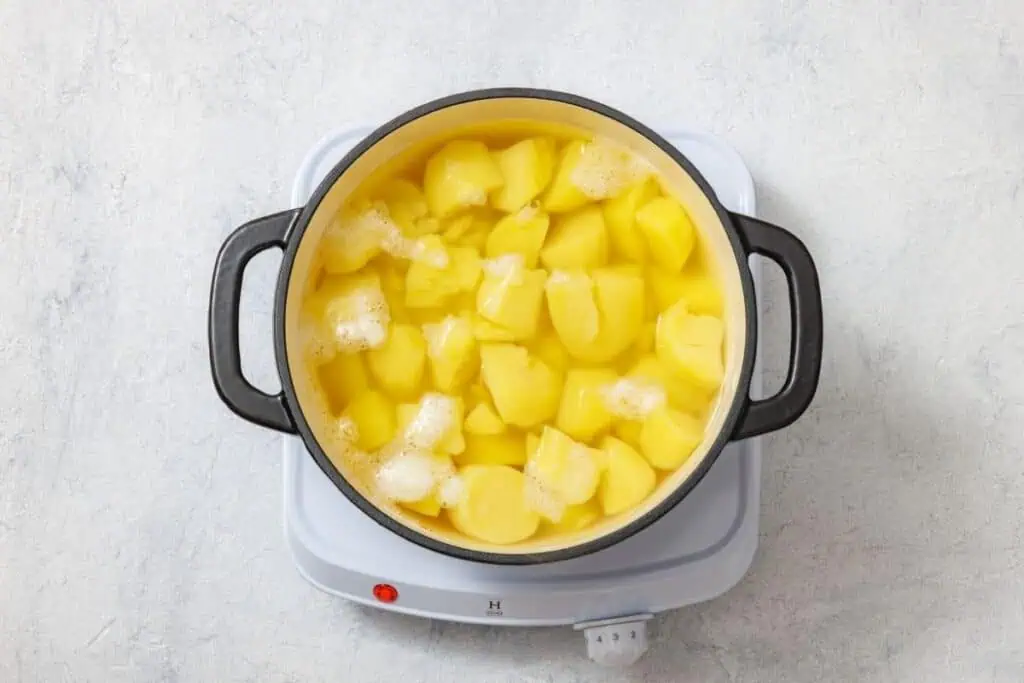 Potatoes boiling in water inside a black cooking pot on an electric stovetop.