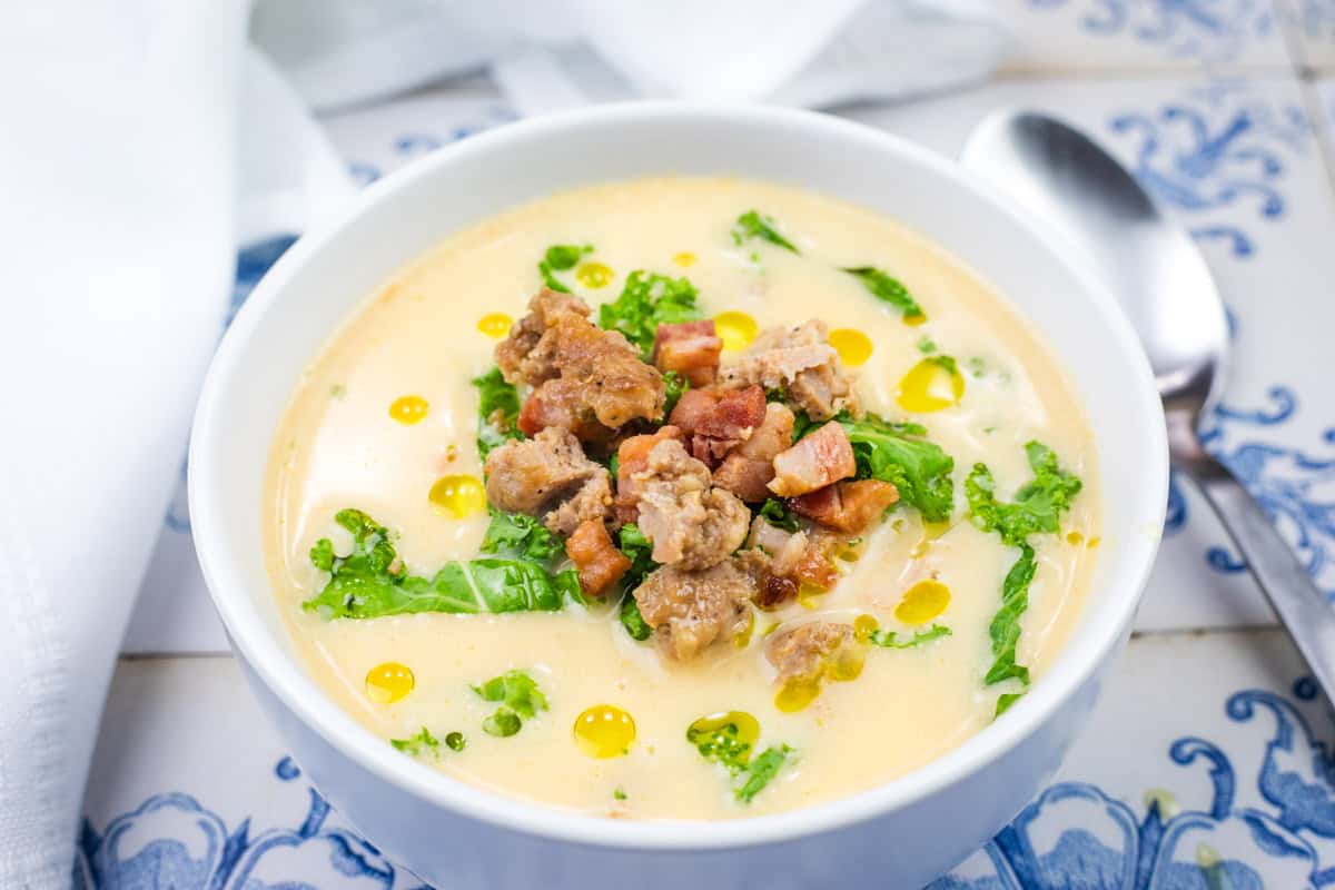 A bowl of Tuscan soup with sausage topped with kale and pancetta pieces in a black soup bowl.