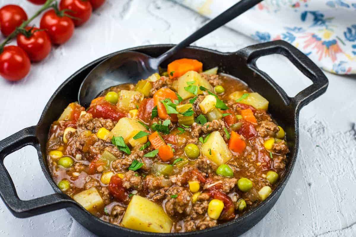 A cast iron skillet filled with Mom&rsquo;s Hamburger Stew garnished with herbs.
