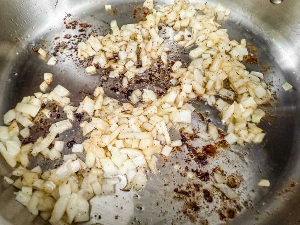 Chopped onions saut&eacute;ing in a stainless steel pan, absorbing the flavorful browned bits left from searing the chicken.