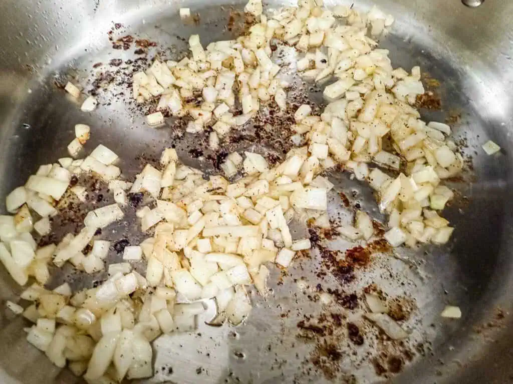 Chopped onions sautéing in a stainless steel pan, absorbing the flavorful browned bits left from searing the chicken.