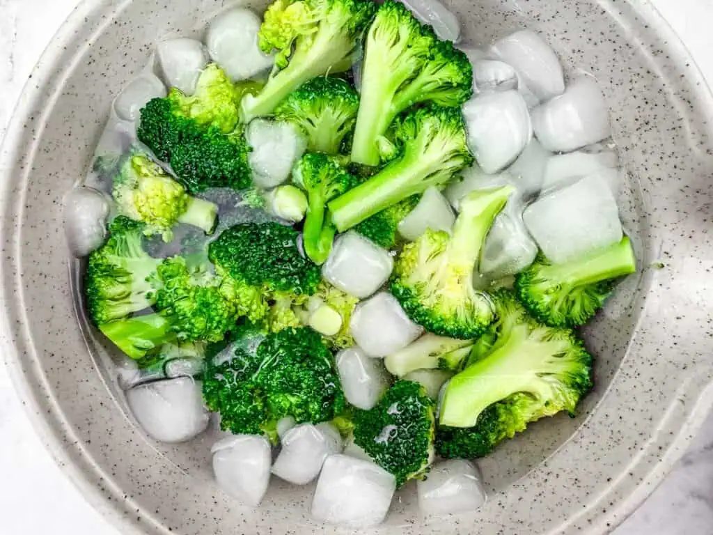 Freshly blanched broccoli florets in an ice water bath to preserve their vibrant green color and crisp texture.