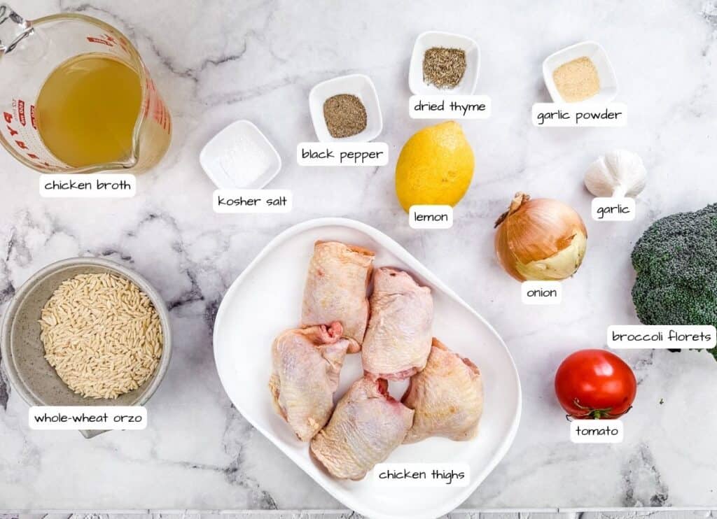 Flat lay of ingredients for Lemon Chicken Orzo Skillet with Broccoli, including chicken thighs, whole-wheat orzo, chicken broth, lemon, onion, garlic, broccoli florets, tomato, and various seasonings, all labeled on a marble countertop.
