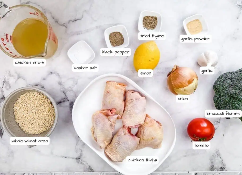 Flat lay of ingredients for Lemon Chicken Orzo Skillet with Broccoli, including chicken thighs, whole-wheat orzo, chicken broth, lemon, onion, garlic, broccoli florets, tomato, and various seasonings, all labeled on a marble countertop.