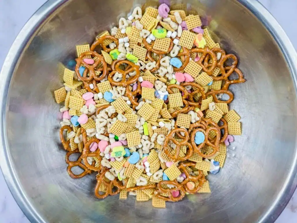 A metal bowl containing a snack mix of pretzels, cereal squares, marshmallows, and colorful cereal pieces.
