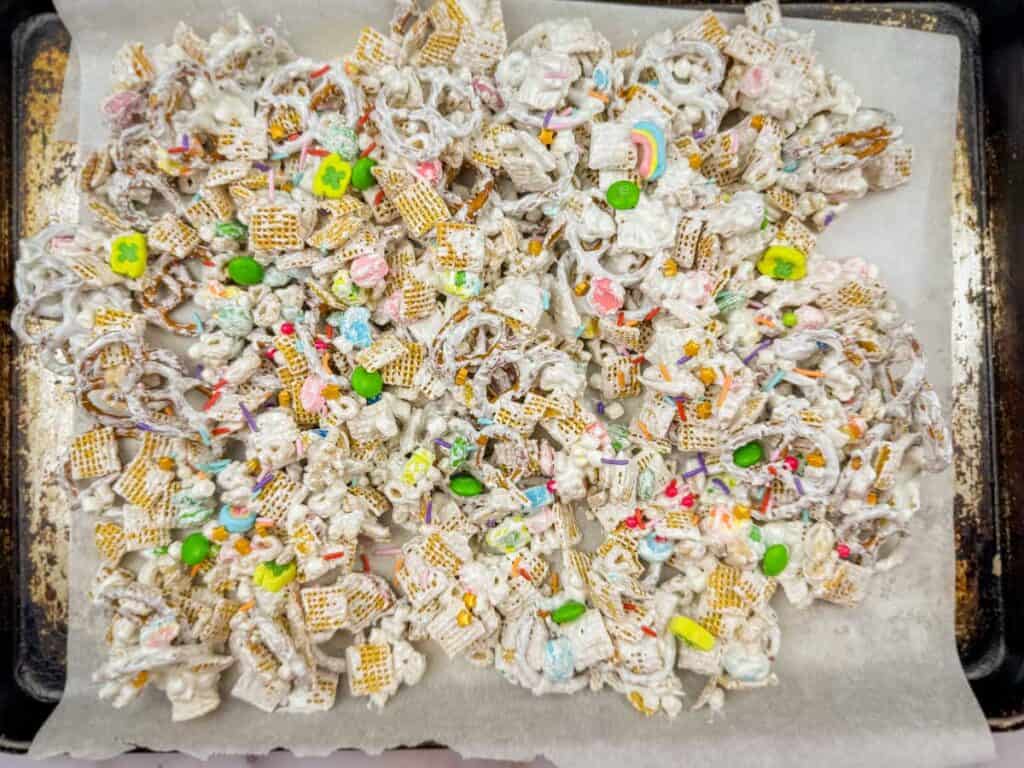 A tray of snack mix with pretzels, cereal, and colorful candies, coated in white confectionery on parchment paper.