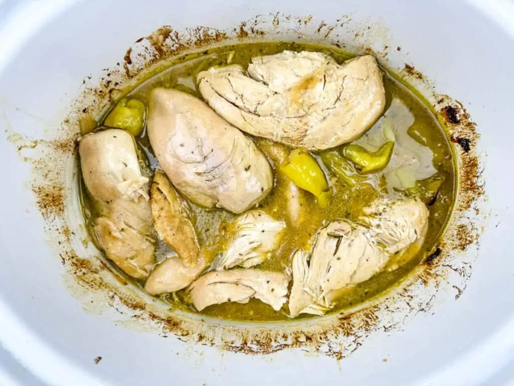 Chicken breasts cooked in broth with pepperoncini peppers in a slow cooker.