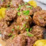 A close-up of Mississippi meatballs, coated in a rich, savory sauce and garnished with pepperoncini peppers fresh chopped parsley.