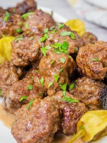 A close-up of Mississippi meatballs, coated in a rich, savory sauce and garnished with pepperoncini peppers fresh chopped parsley.