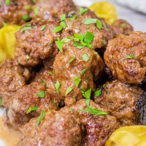 A close-up of Mississippi meatballs, coated in a rich, savory sauce and garnished with pepperoncini peppers fresh chopped parsley.