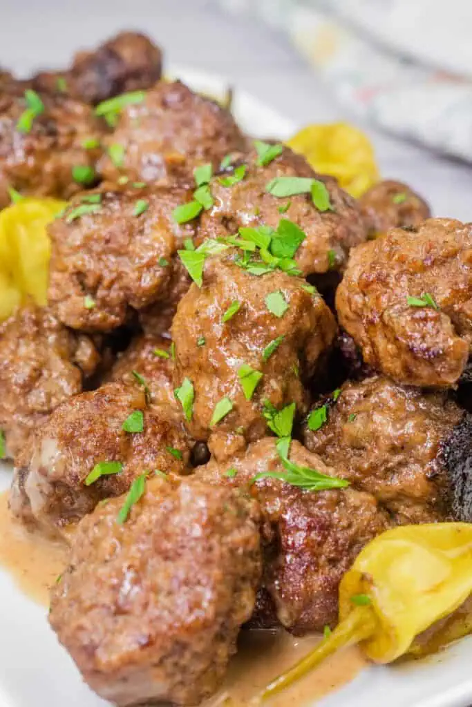 A close-up of Mississippi meatballs, coated in a rich, savory sauce and garnished with pepperoncini peppers fresh chopped parsley.