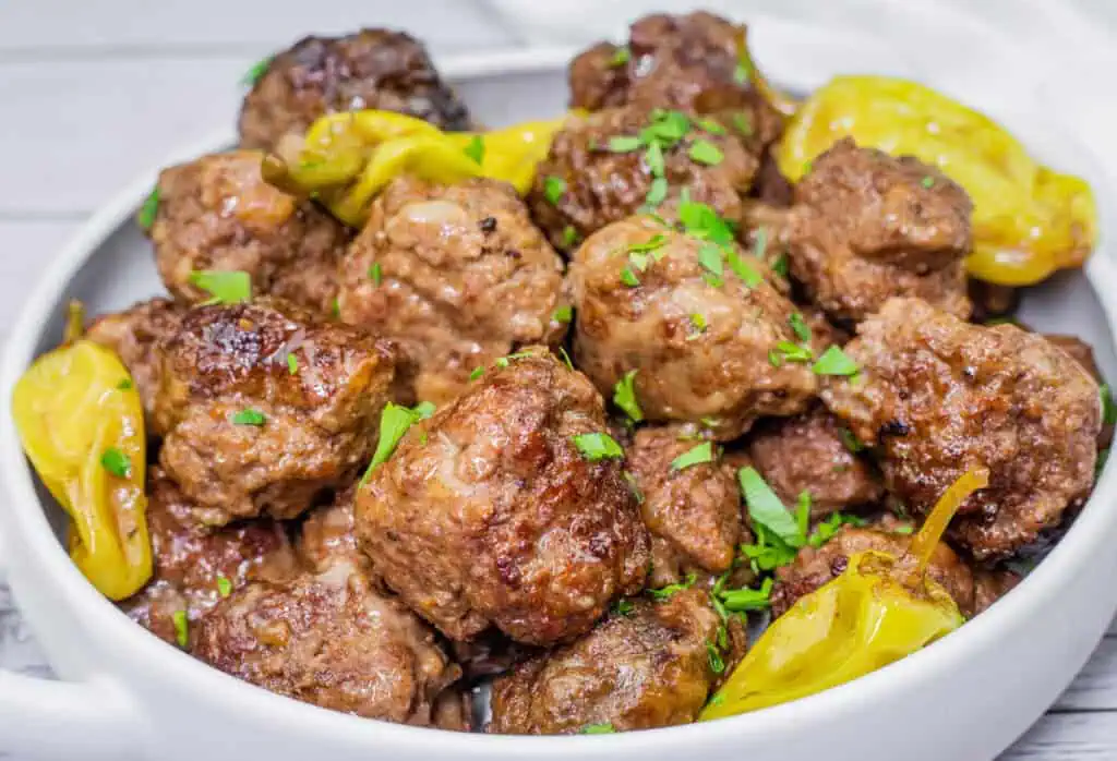 Mississippi meatballs served in a bowl, garnished with fresh parsley and pepperoncini peppers for a flavorful finish.