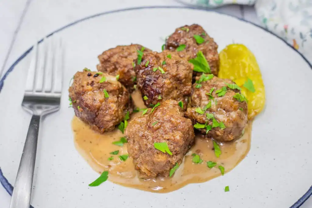 Mississippi meatballs served on a plate with rich gravy, garnished with fresh parsley and a pepperoncini pepper.