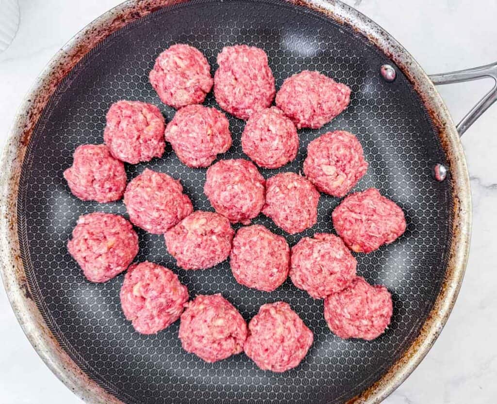 Raw meatballs arranged in a single layer in a non-stick frying pan, ready to be browned before further cooking.