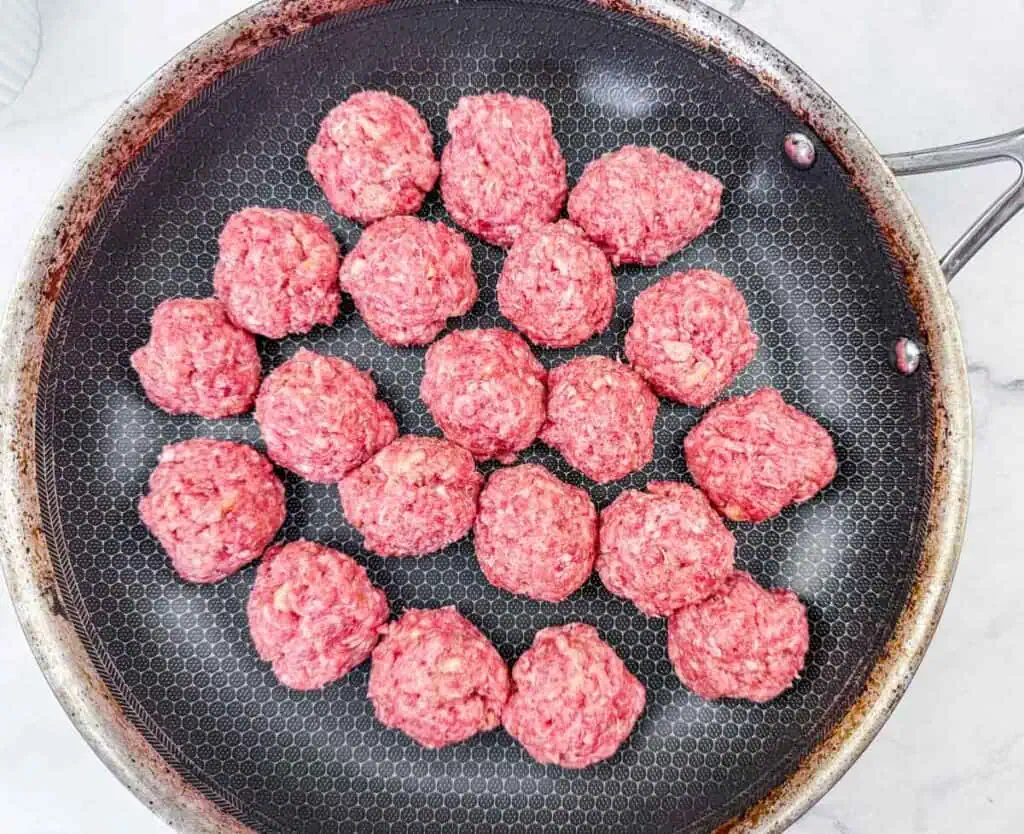 Raw meatballs arranged in a single layer in a non-stick frying pan, ready to be browned before further cooking.