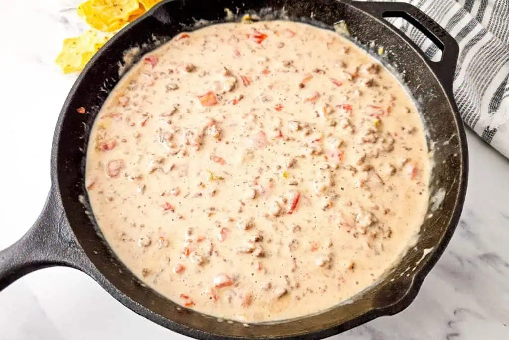 A cast iron skillet filled with creamy Queso Blanco Rotel Dip, likely a queso dip, with tortilla chips in the background on a marble surface.