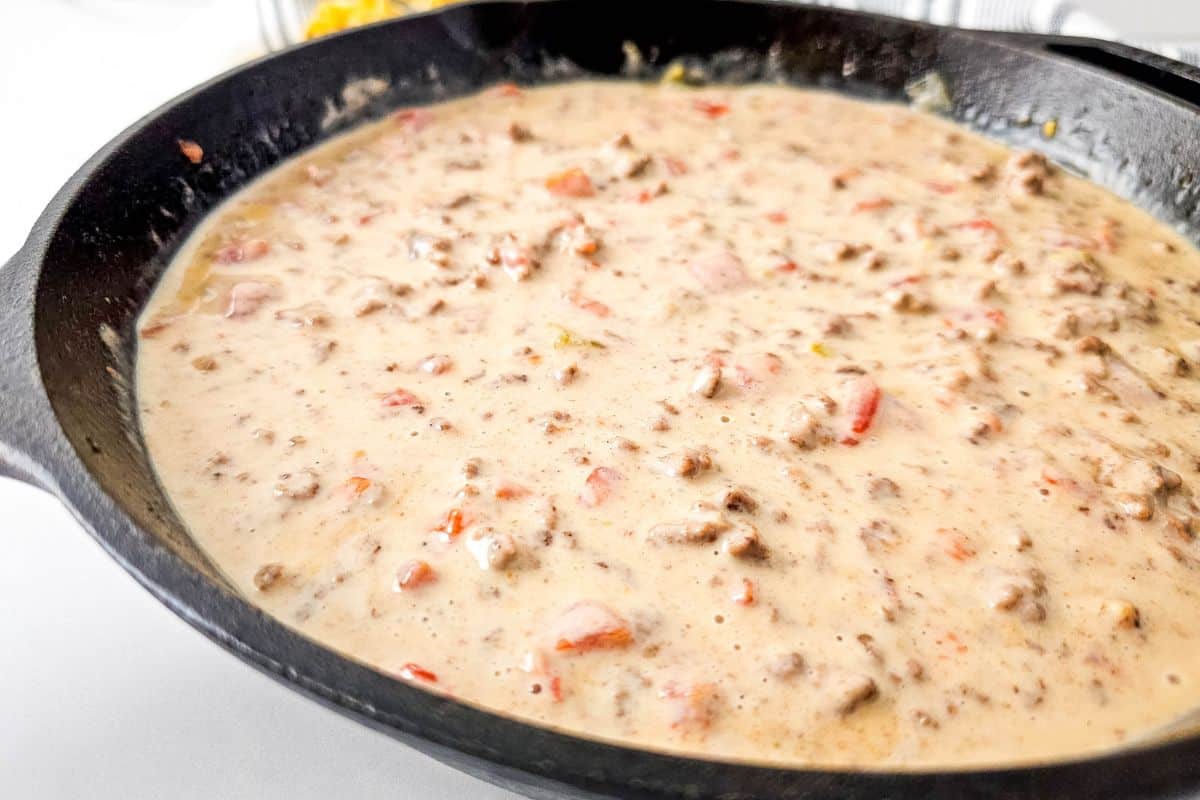 A skillet filled with creamy Queso Blanco Rotel Dip containing ground meat and diced tomatoes.