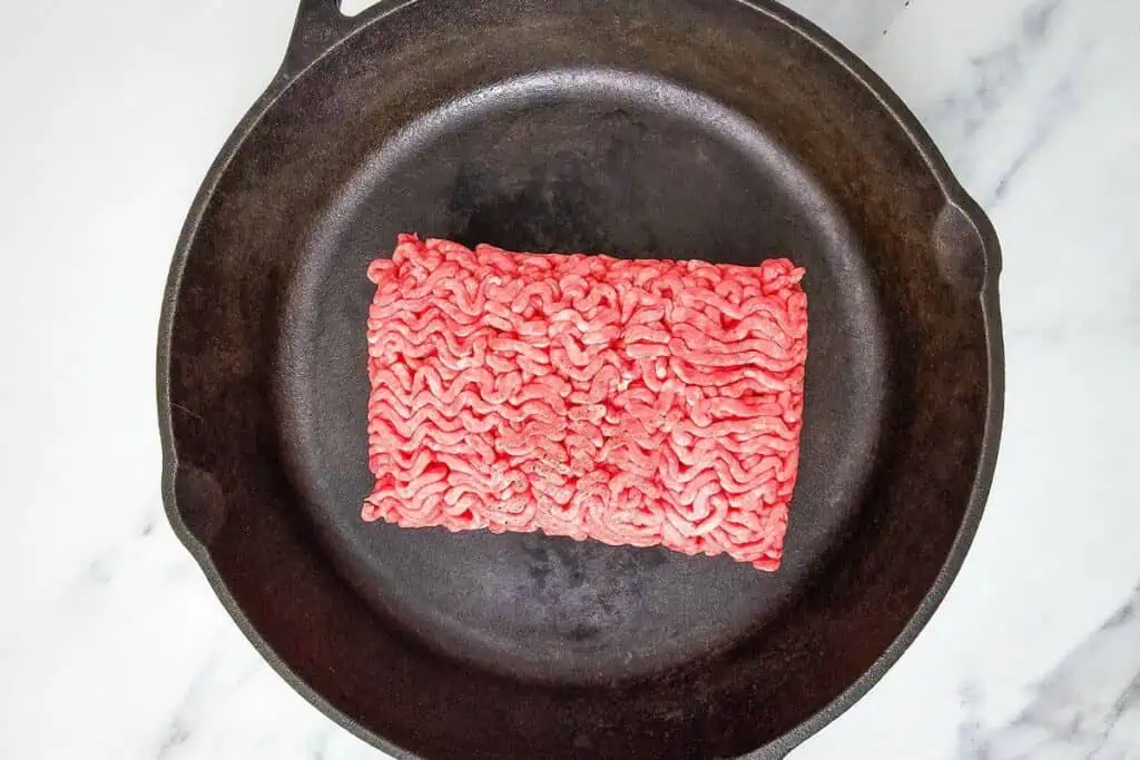Ground beef placed in a black cast iron skillet on a marble surface.