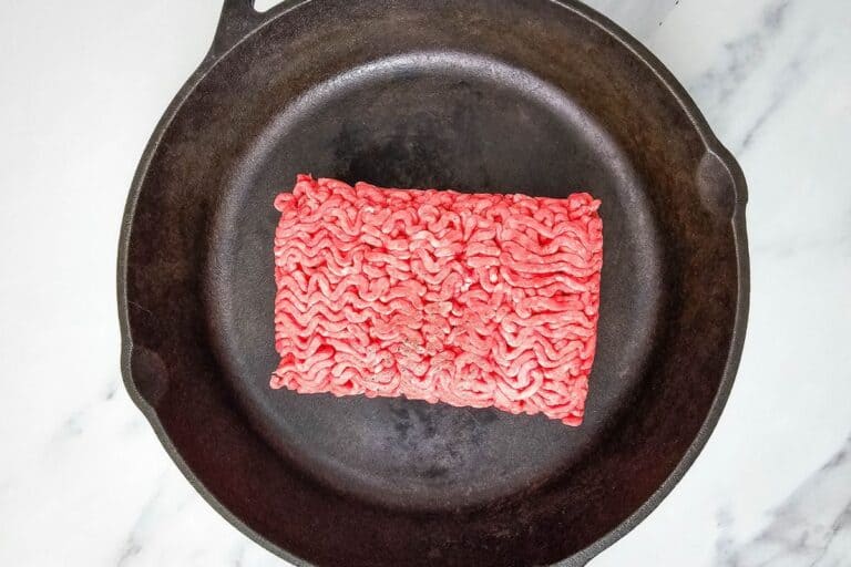 Ground beef placed in a black cast iron skillet on a marble surface.