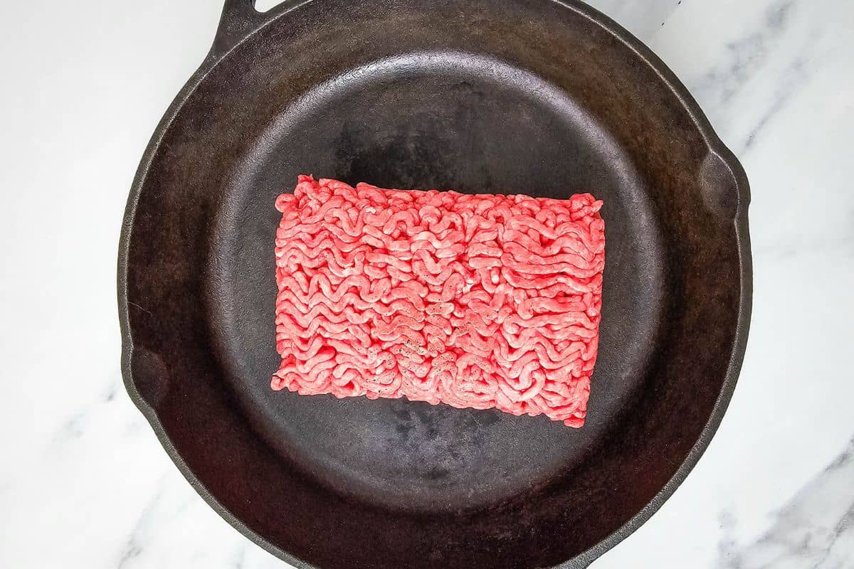 Ground beef placed in a black cast iron skillet on a marble surface.