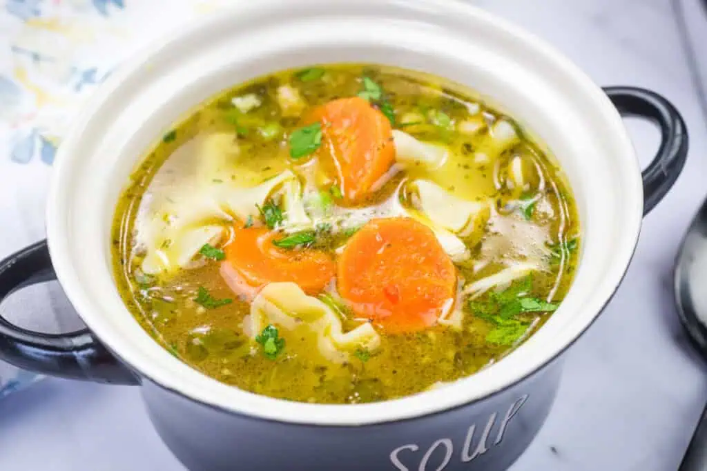Bowl of Rotisserie Chicken Noodle Soup with carrots, peas, and herbs in a ceramic bowl.