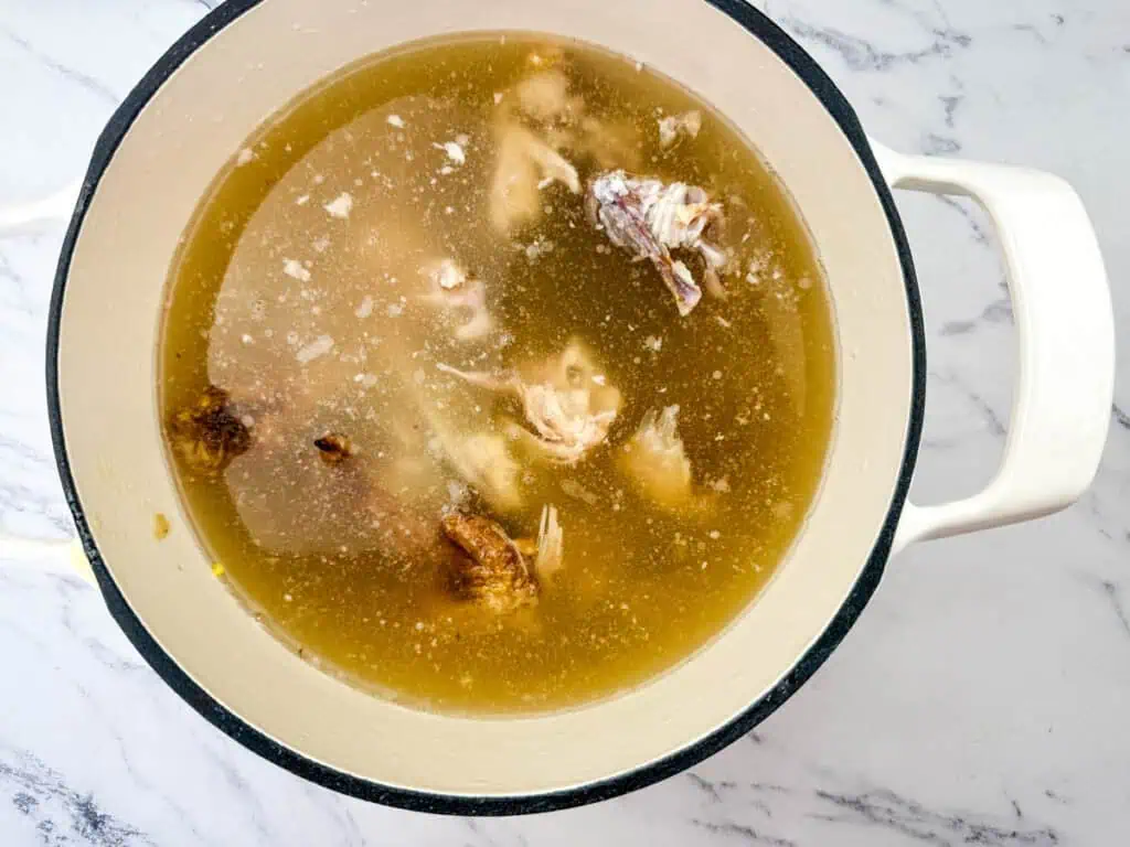 A white pot filled with chicken bones and broth on a marbled surface.