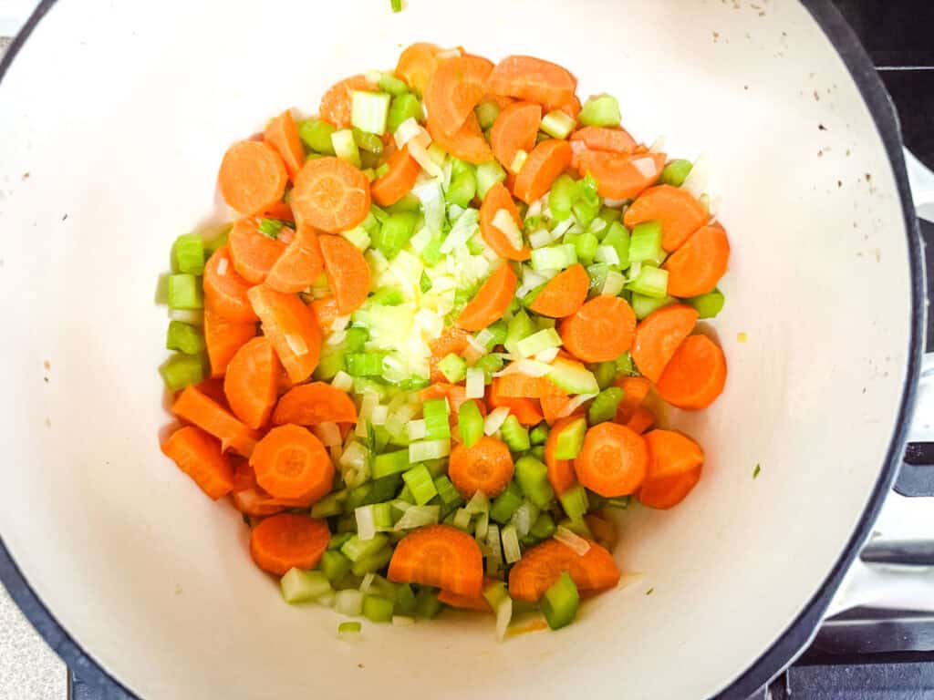 Chopped carrots and celery in a white pot on a stove, ready to cook.