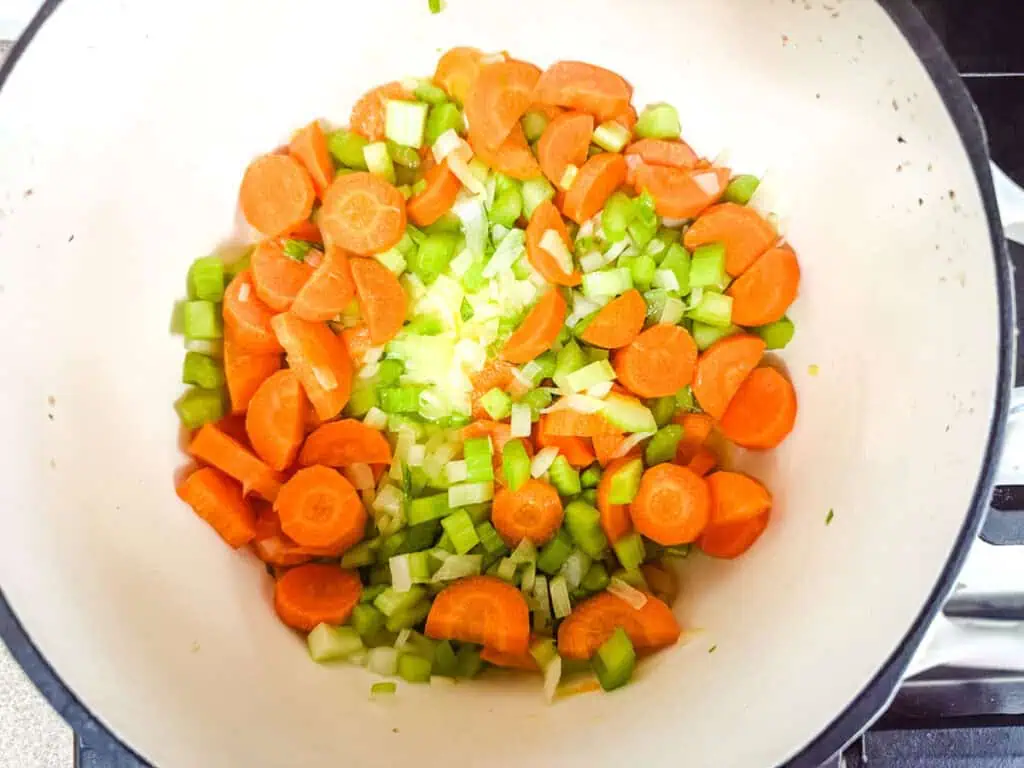 Chopped carrots and celery in a white pot on a stove, ready to cook.