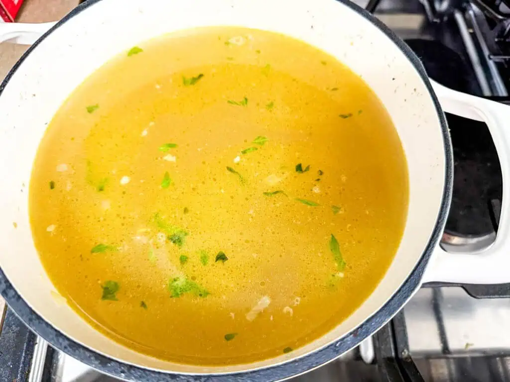 A white pot containing yellow broth with visible herbs and pieces on a stove.