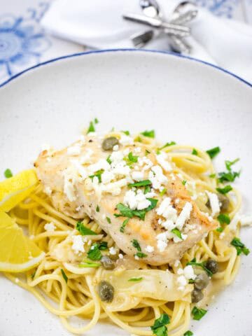 A pasta topped with a Skillet Chicken with Artichokes, Lemon, and Feta on a round plate.