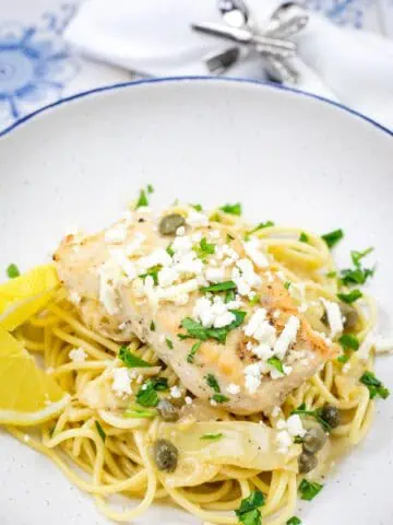 A pasta topped with a Skillet Chicken with Artichokes, Lemon, and Feta on a round plate.