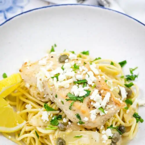 A pasta topped with a Skillet Chicken with Artichokes, Lemon, and Feta on a round plate.