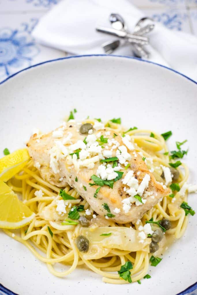 A pasta topped with a Skillet Chicken with Artichokes, Lemon, and Feta on a round plate.