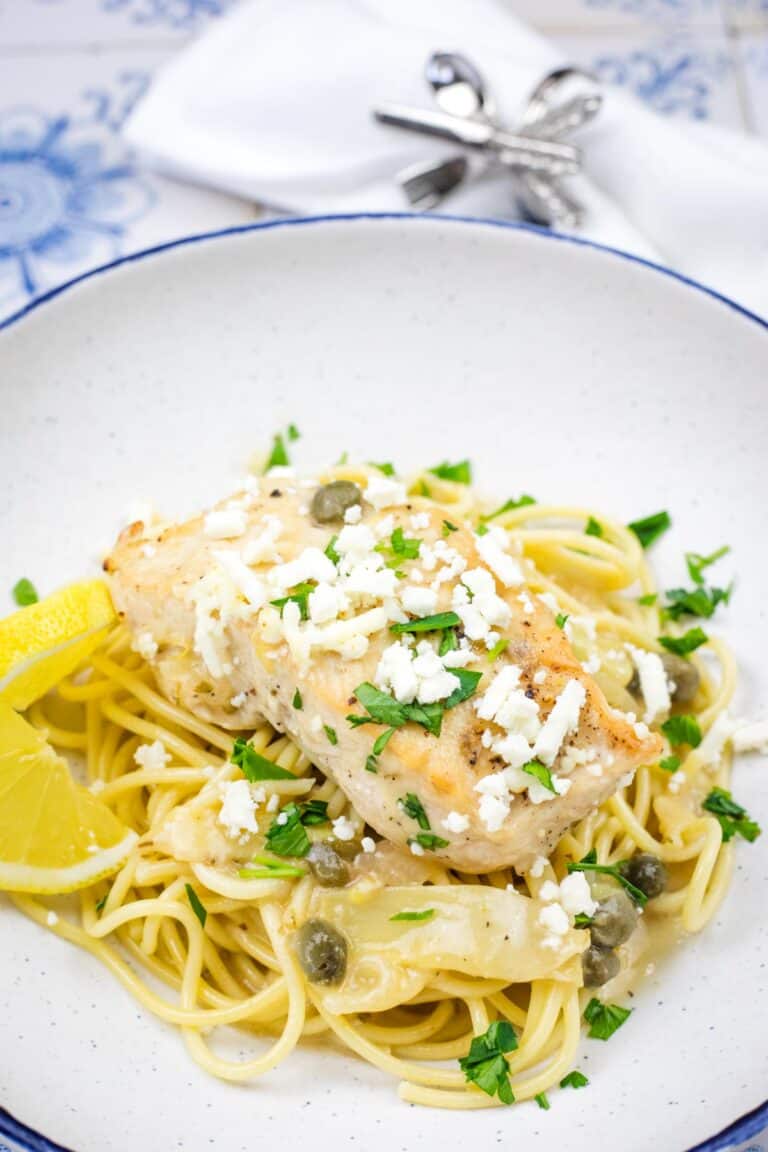 A pasta topped with a Skillet Chicken with Artichokes, Lemon, and Feta on a round plate.
