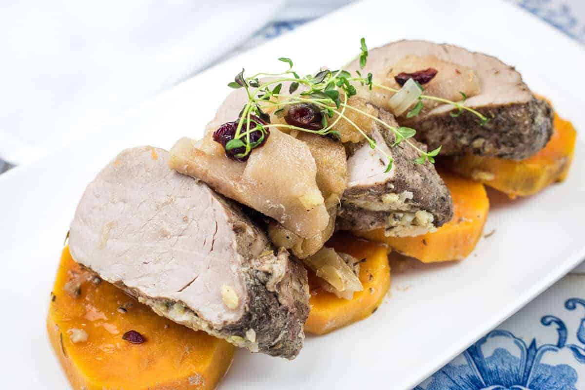 Sliced slow cooker pork roast with sweet potatoes & apples on a white plate.