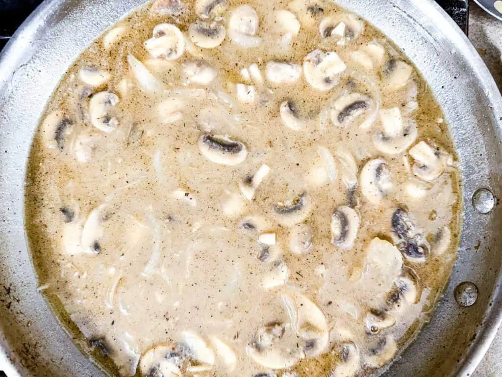 A skillet filled with creamy mushroom sauce, featuring sliced mushrooms and onions in a thick, beige liquid.
