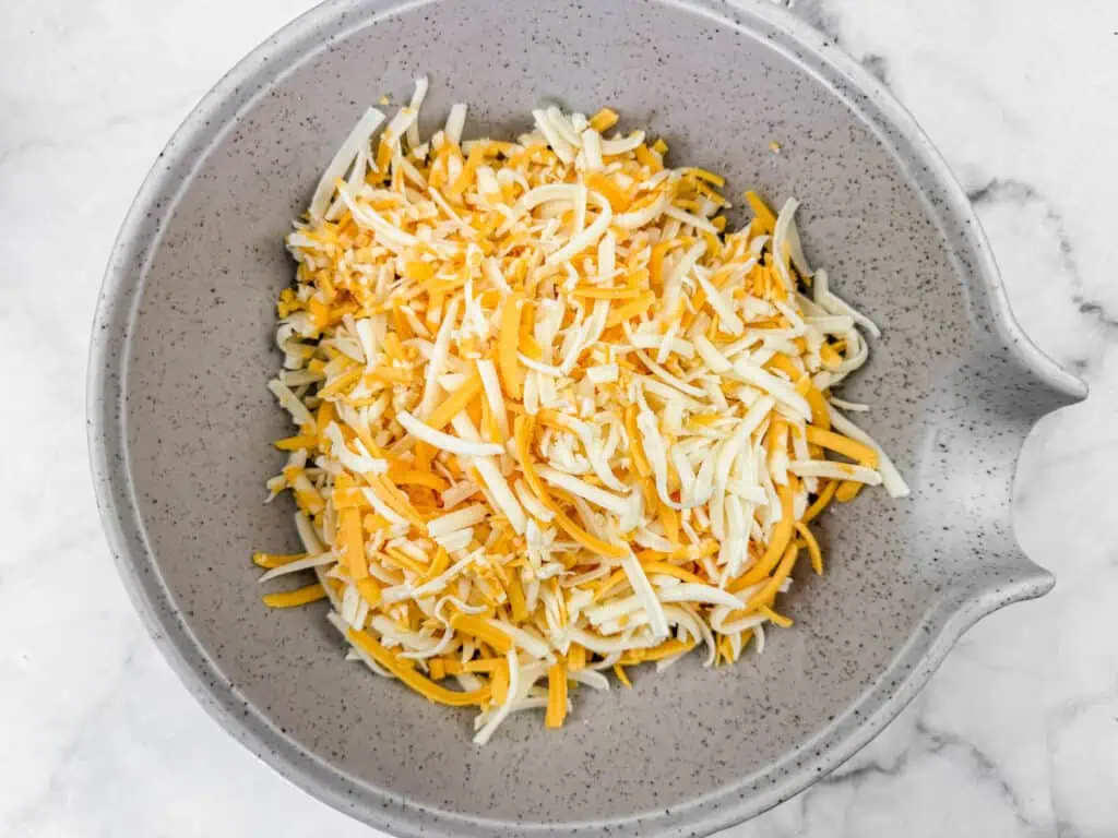 A gray bowl filled with a mix of shredded cheese on a marble surface.