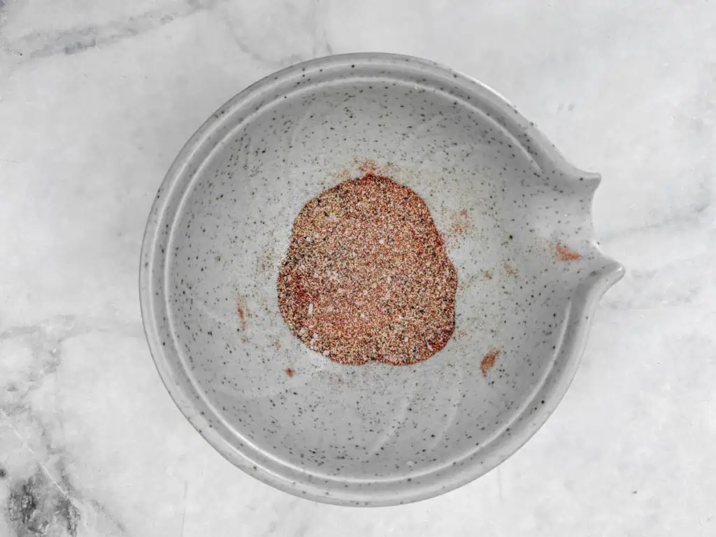 A small gray bowl on a marble surface containing a mixed spice blend.
